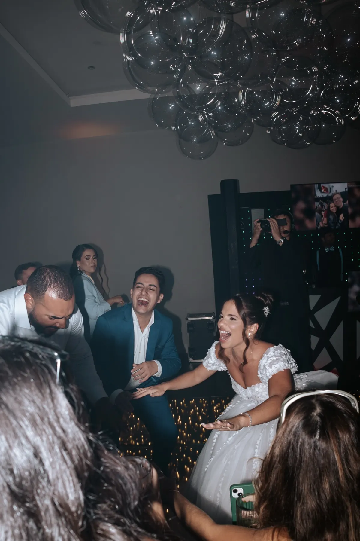 Noiva ri e dança junto dos convidados, sob uma instalação de globos transparentes.